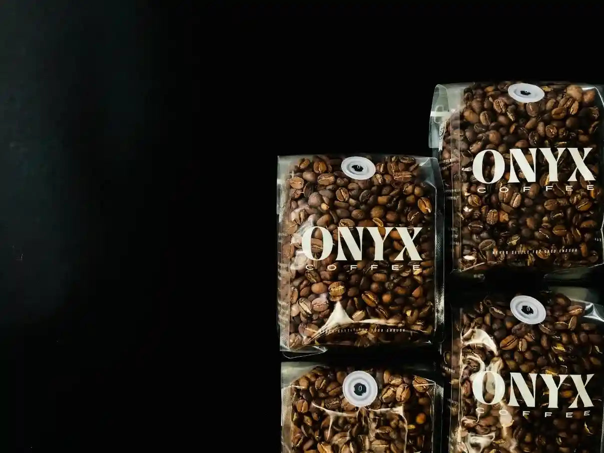 Przezroczyste opakowania kawy specialty Onyx Coffee Lab na czarnym tle. Białe napisy. Boczne oświetlenie.